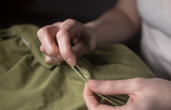 moda sustentável: Mãos femininas com agulha e linha para consertar roupas, close-up.