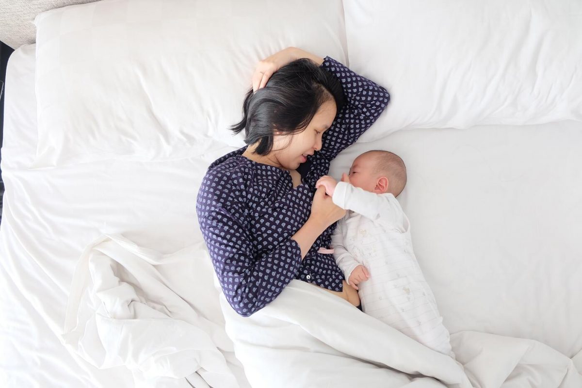Mãe e bebê asiáticas deitadas na cama ilustrando a privação de sono na maternidade