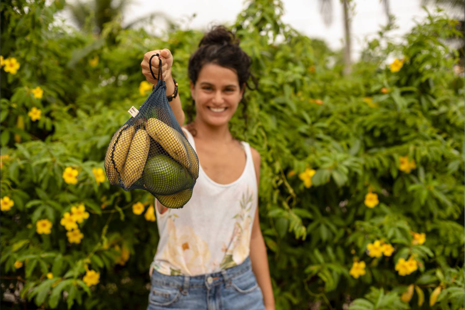 pessoa segurando um saco de rede de pesca reciclado da Positiv.a contendo frutas