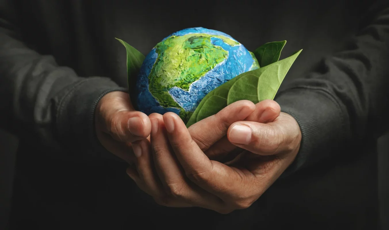 Homem segurando o planeta terra com folhas entre o planeta e as mãos, representando o eco friendly
